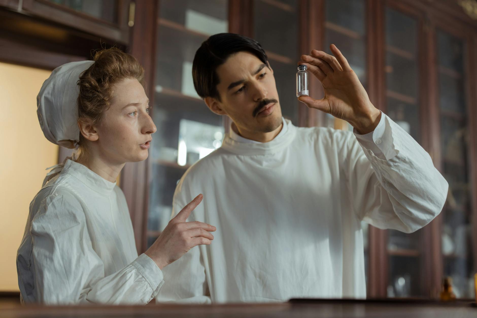 Badacze w XIX‑wiecznym laboratorium oglądają fiolkę z lekarstwem