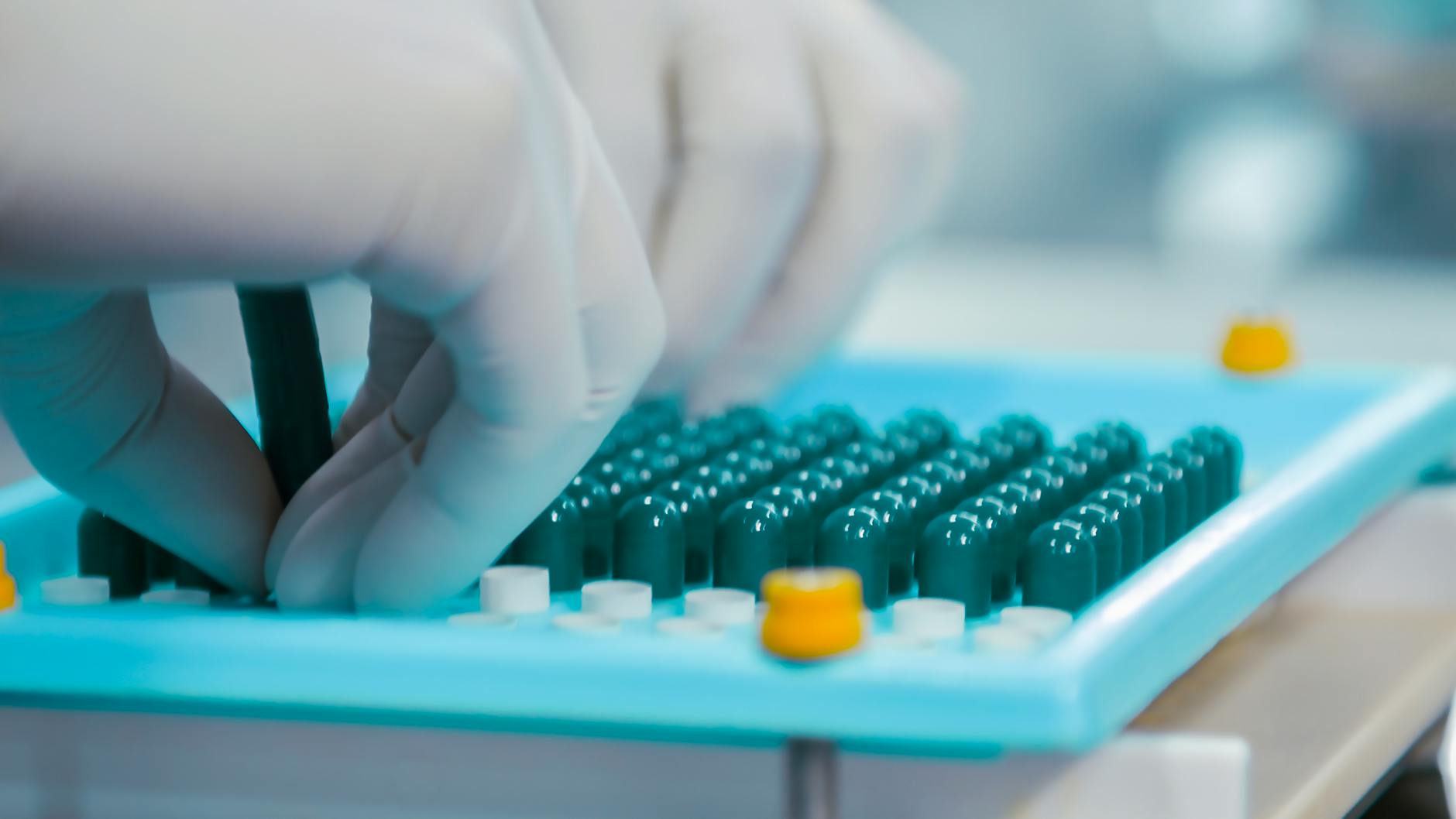 Ręce w rękawiczkach sortują kapsułki w laboratorium farmaceutycznym