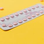 Blister różowych tabletek antykoncepcyjnych na żółtym tle