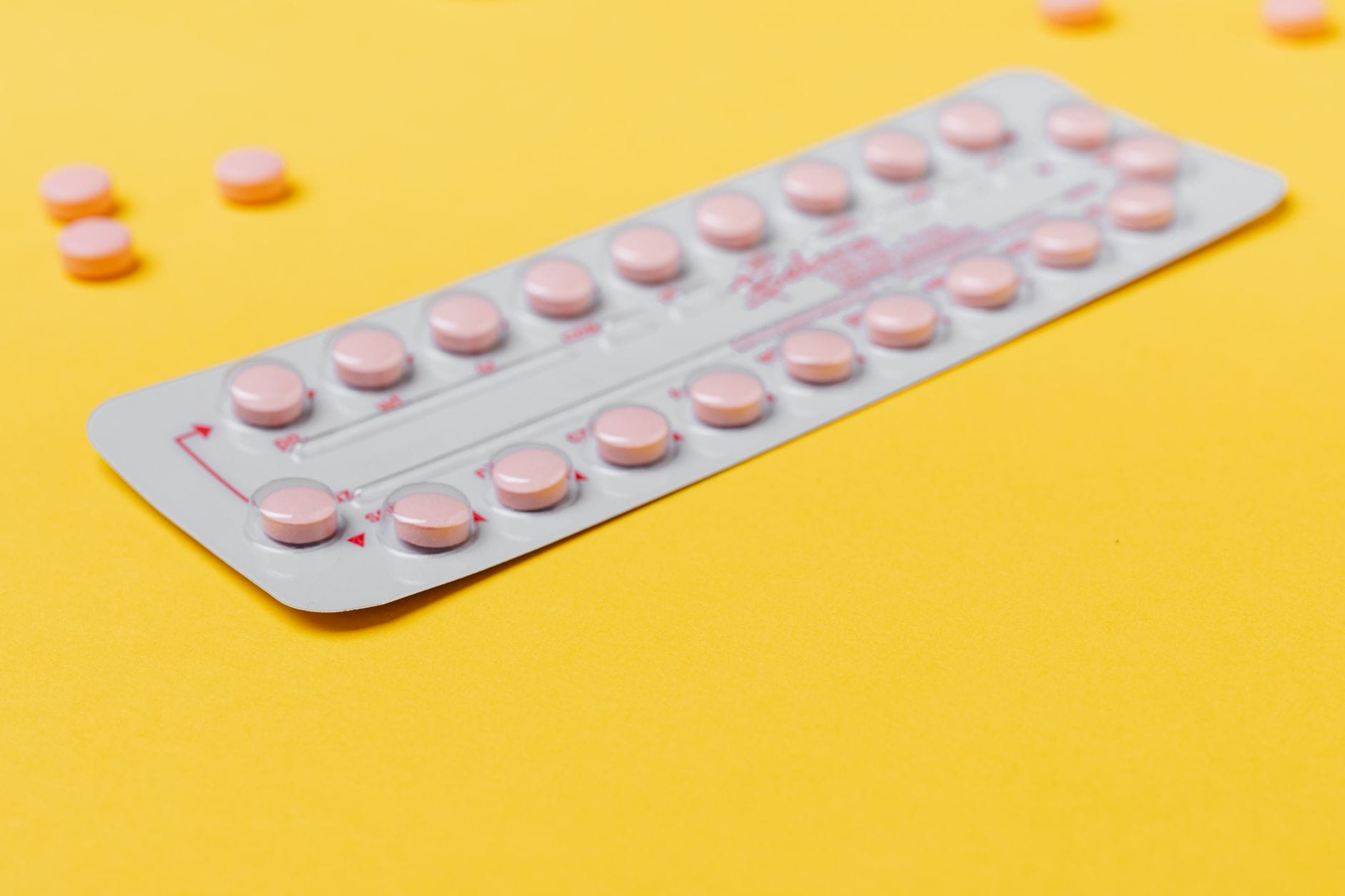 Blister różowych tabletek antykoncepcyjnych na żółtym tle