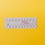 Blister różowych tabletek antykoncepcyjnych na żółtym tle