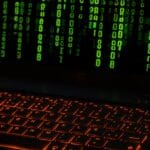 Klawiatura laptopa z pomarańczowym podświetleniem i zielonym kodem na ekranie
