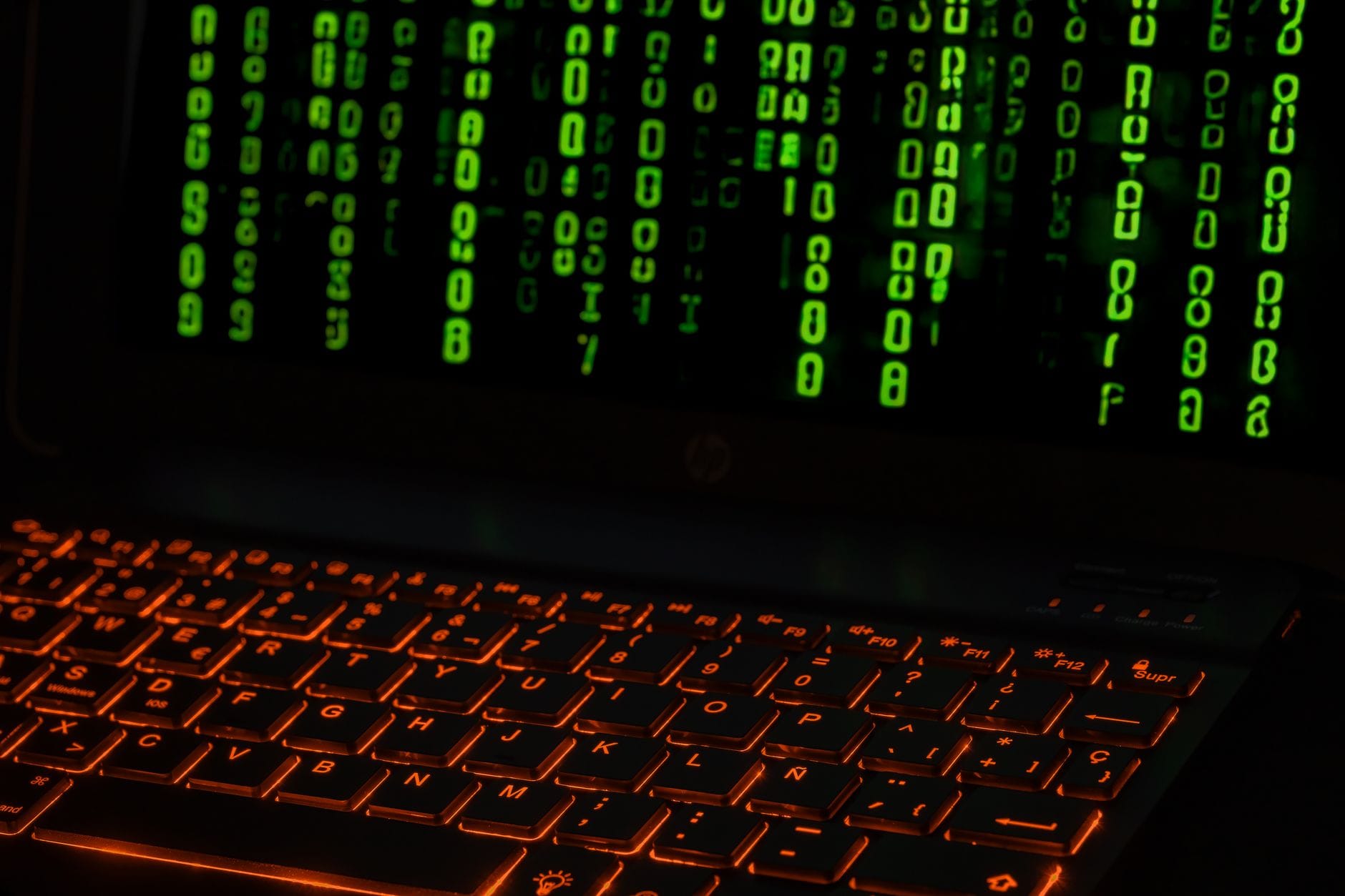 Klawiatura laptopa z pomarańczowym podświetleniem i zielonym kodem na ekranie