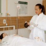 Noworodek i młoda mama na sali szpitalnej z personelem medycznym