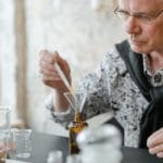 Starsza osoba miesza olejki w brązowych butelkach w przytulnym wnętrzu